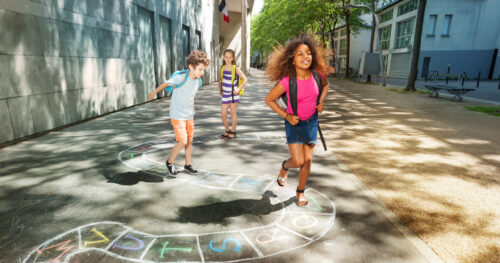 Group of kids jumping and paying hopscotch game outside near the school together